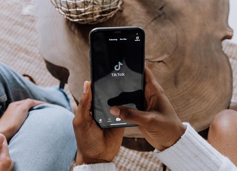 Two hands holding a mobile phone with TikTok displayed on the screen.